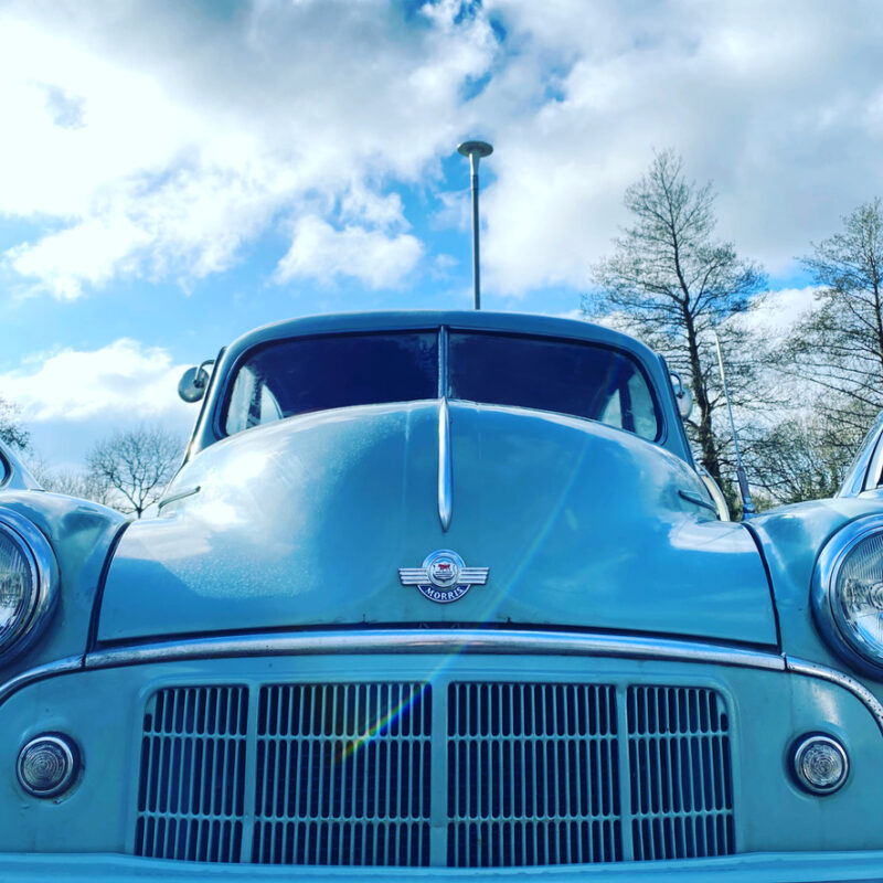 Blue Morris Minor car, under blue sky